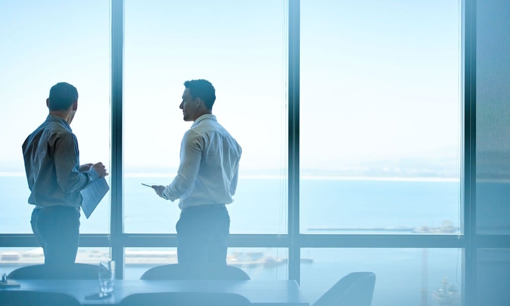 Two men stand at a window in a conference room
