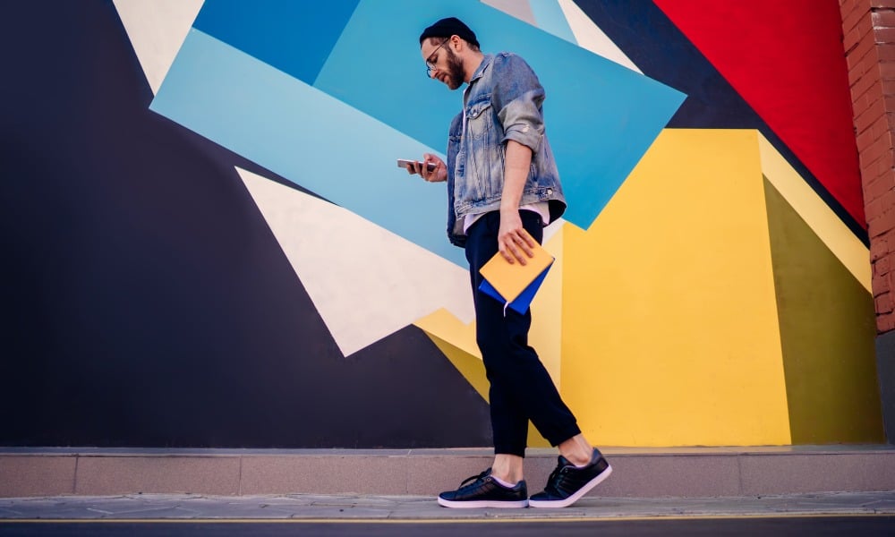 A man walks with his phone in front of a colorful mural