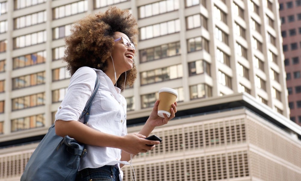Woman walks down the street listening to music and holding a cup of coffee.