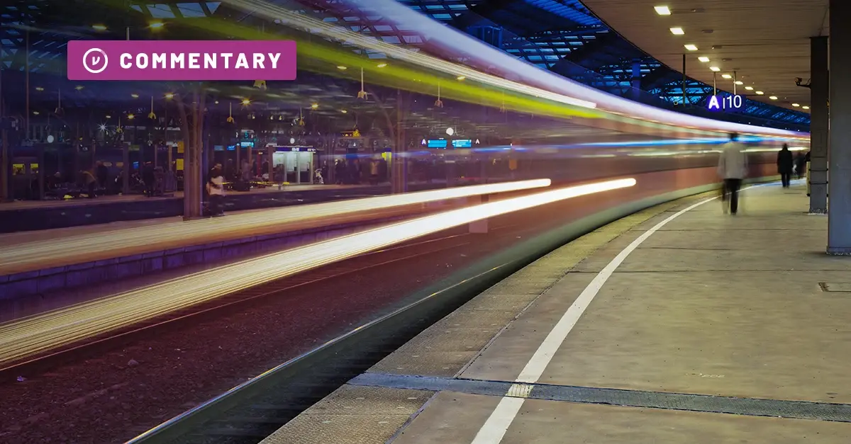 A train moves swiftly past a station platform at night. 