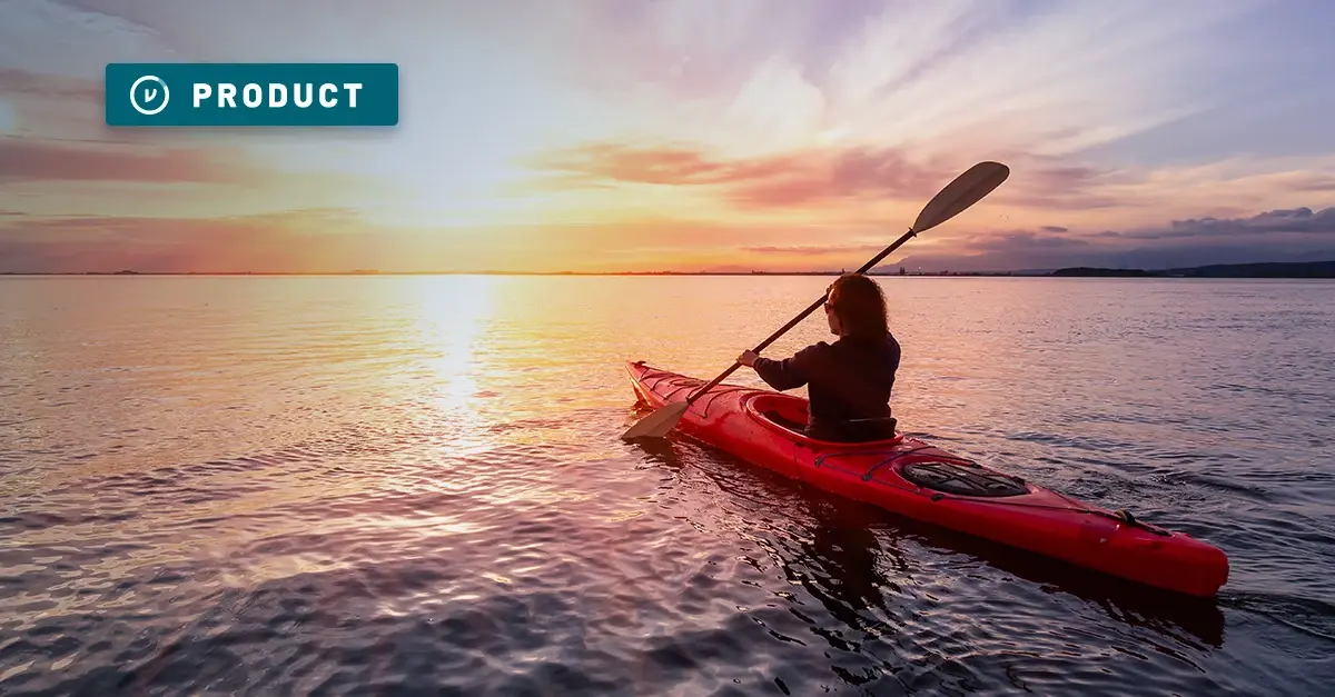 A woman paddles a red kayak in a sound at sunset.