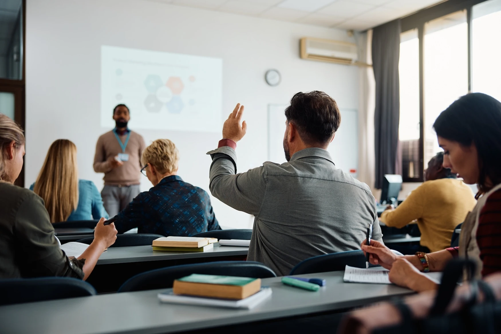 A college student raises his hand in a classroom