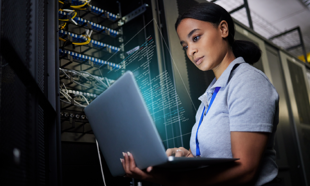 A woman uses her laptop in a data center in front of a server.