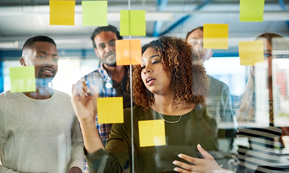 A team uses post-it notes to collaborate on a glass wall. 