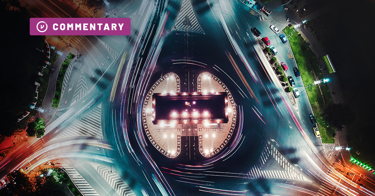 birdseye view of city roundabout at night; lights stretch across the road in long exposure as cars make their way around the bend