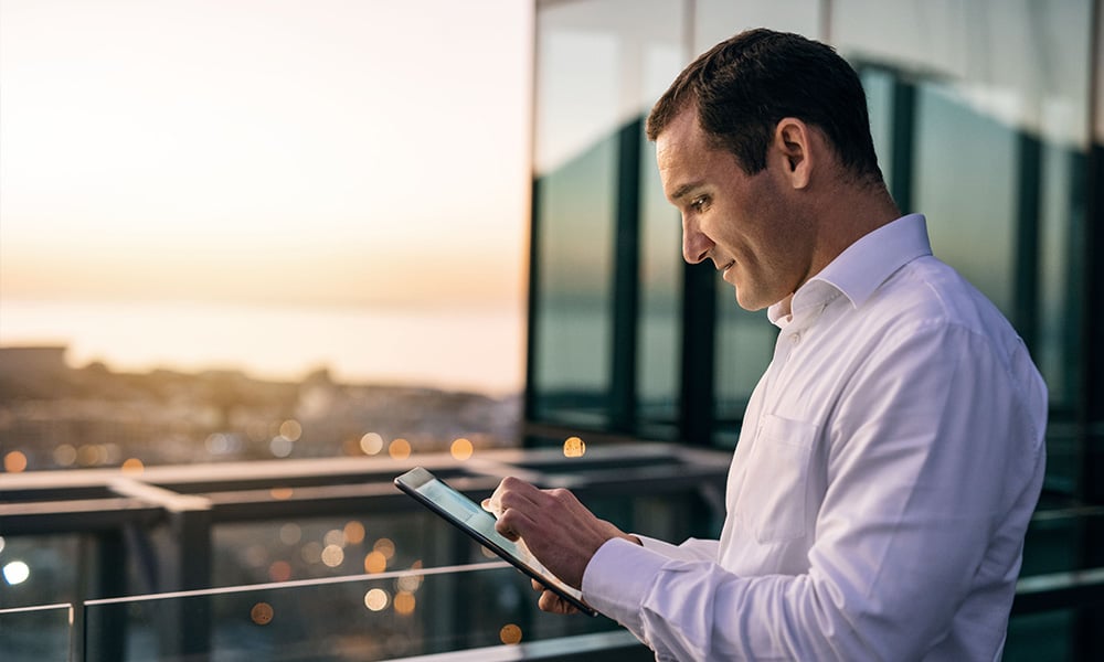 A man stands on a balcony viewing data on a tablet.